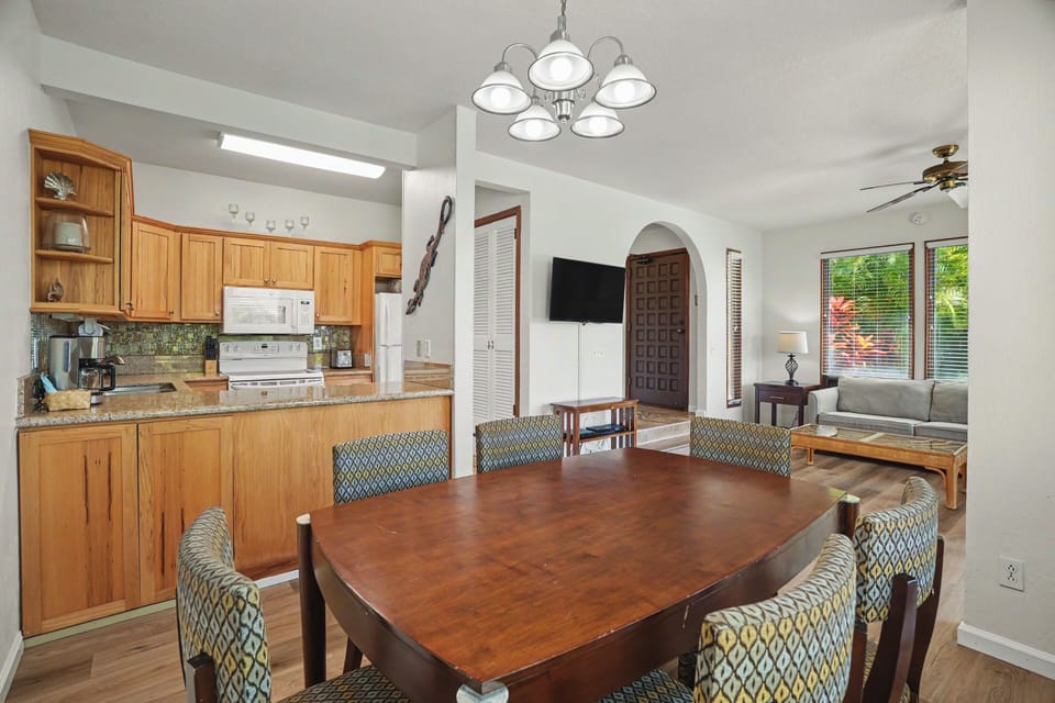 You'll love gathering around this spacious dining table, perfectly positioned between a well-equipped kitchen and cozy living area. Natural light pours in through large windows, creating a warm, inviting atmosphere for meals and conversation.