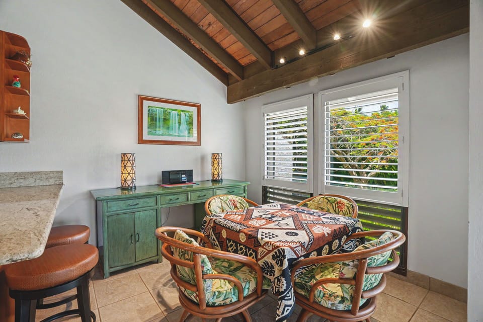 Gather around this charming dining space with vaulted wood-beam ceilings and plantation shutters framing tropical views—your perfect spot for morning coffee or evening meals.
