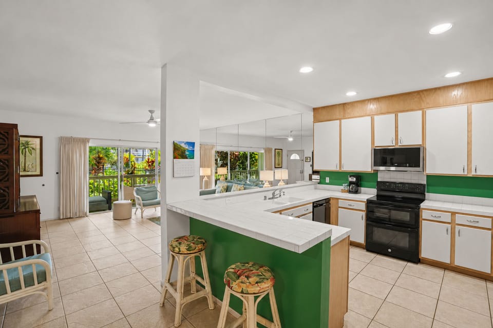 Gather around the bright, tropical kitchen island for morning coffee or meal prep—your home base flows seamlessly into the breezy living area and lush garden views beyond.