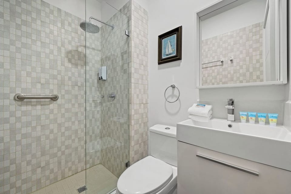 Serene bathroom featuring a walk-in glass shower and fresh, clean tiles - Enjoy thoughtful touches like soft towels and charming nautical artwork for a relaxing vibe - A sleek vanity and modern fixtures ensure a convenient and pleasant experience