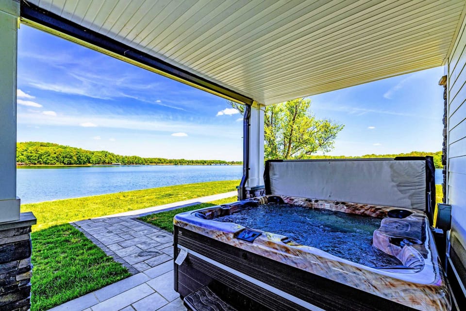 Hot Tub - Lakefront soak under a covered porch, paver patio underfoot, open water just past the grass. Front-row seat, no audience.