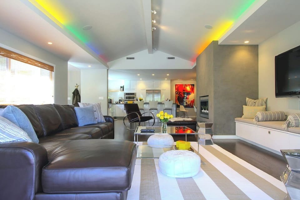 Relax in this stylish, open-concept living space with a cozy fireplace, sleek leather sofa, and modern kitchen. Vaulted ceilings and built-in window seating create a bright, inviting vibe. The perfect spot to lounge, gather, and feel right at home!