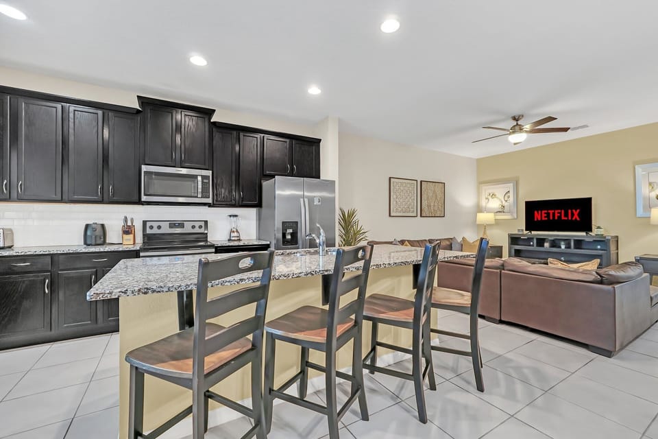 Modern kitchen with granite countertops and a breakfast bar overlooking the living area with a smart TV.