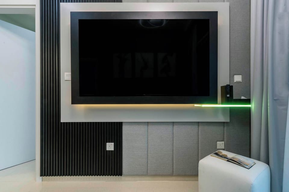 Enjoy sleek entertainment in this modern lounge featuring a wall-mounted TV, ambient lighting, and minimalist design. A stylish space for relaxing nights and urban comfort.