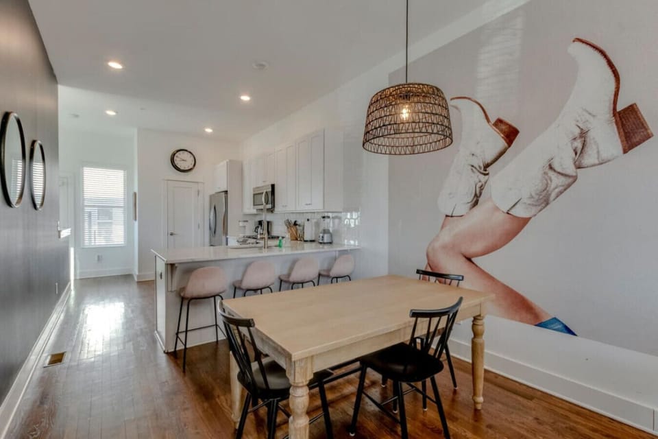 Dining area with farmhouse table, black chairs, wicker pendant, and kitchen visible