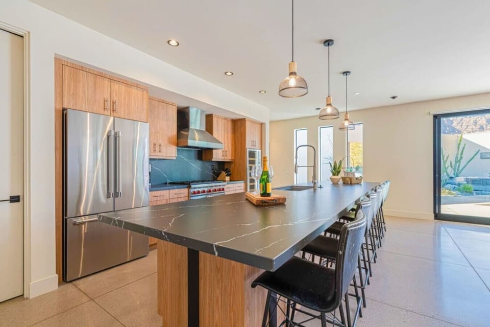Kitchen w/ long island, bar stools for six, stainless fridge & pendant lights.
