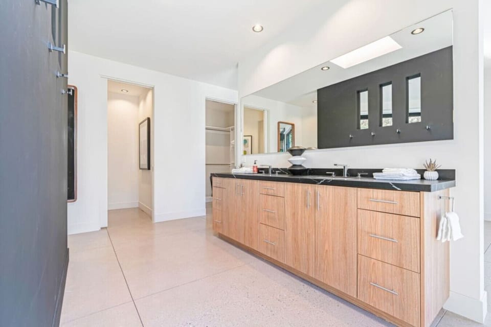 En suite vanity w/ wood cabinetry, dark stone counter and a glass walk-in shower.
