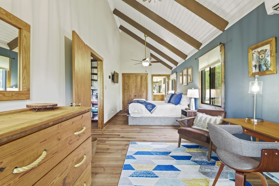 The vaulted beam bedroom doubles as a workspace with a desk and reading chair. A rope handled dresser adds chalet character.
