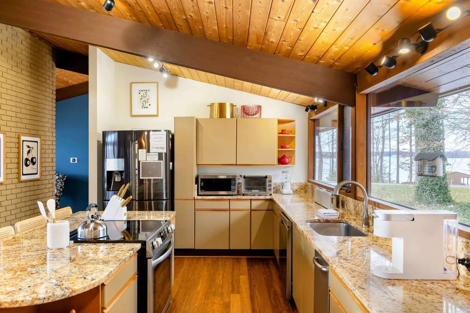 The kitchen combines functionality and elegance with its sleek cabinetry, granite countertops, and stainless steel appliances, all framed by stunning lake views through large windows.