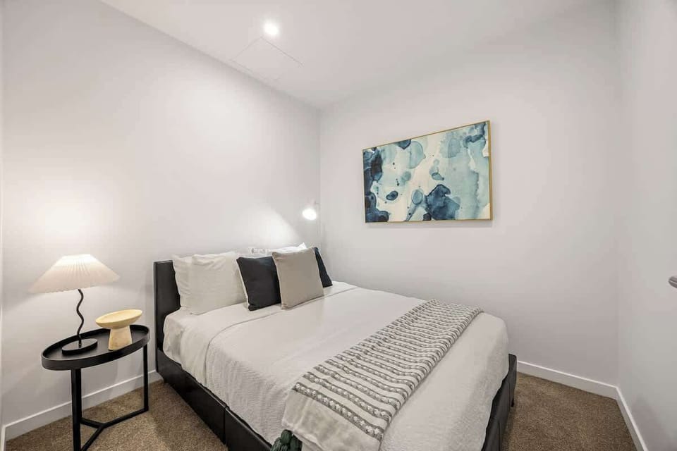 Comfortable bedroom with a neatly made bed, soft carpet, and simple, modern styling. Gentle lighting and calm tones create a quiet space designed for restful sleep and relaxed evenings.
