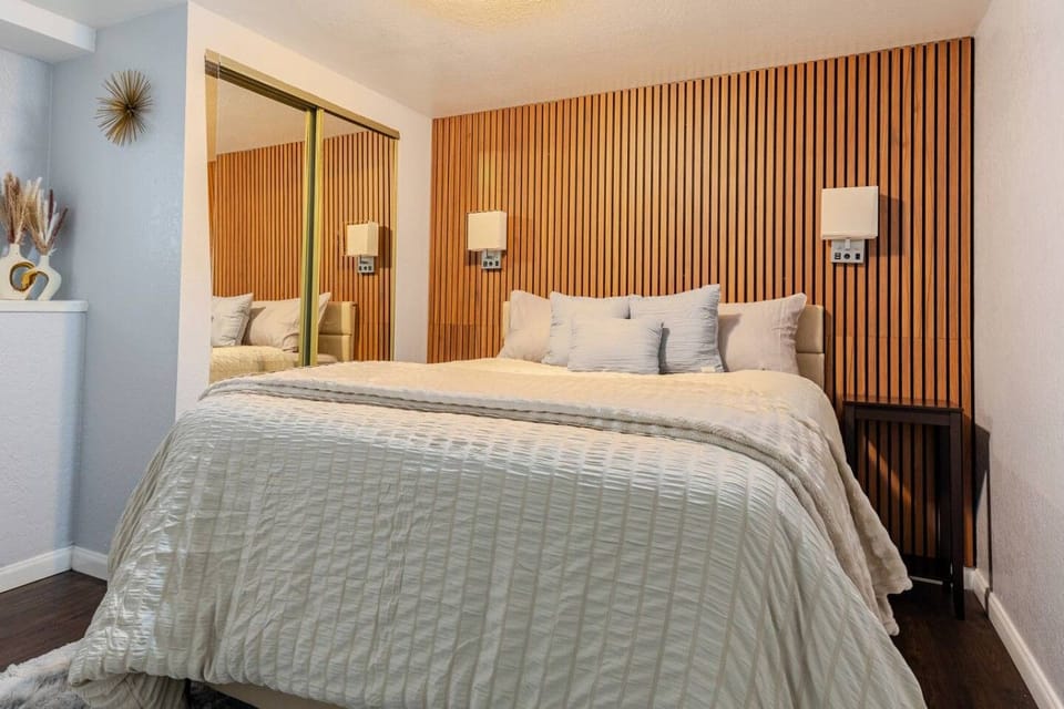 Primary bedroom with wood accent wall, reading lights, and mirrored closet