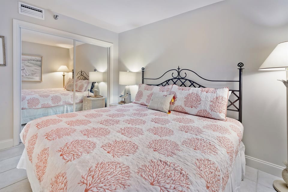 Sink into your cozy bedroom retreat with coral-patterned bedding and elegant black iron headboard, perfectly cooled by air conditioning for restful nights.