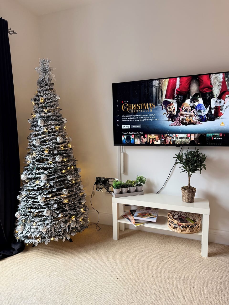 Festive living room featuring a beautifully decorated Christmas tree and a wall-mounted smart TV with access to Netflix, perfect for cozy evenings