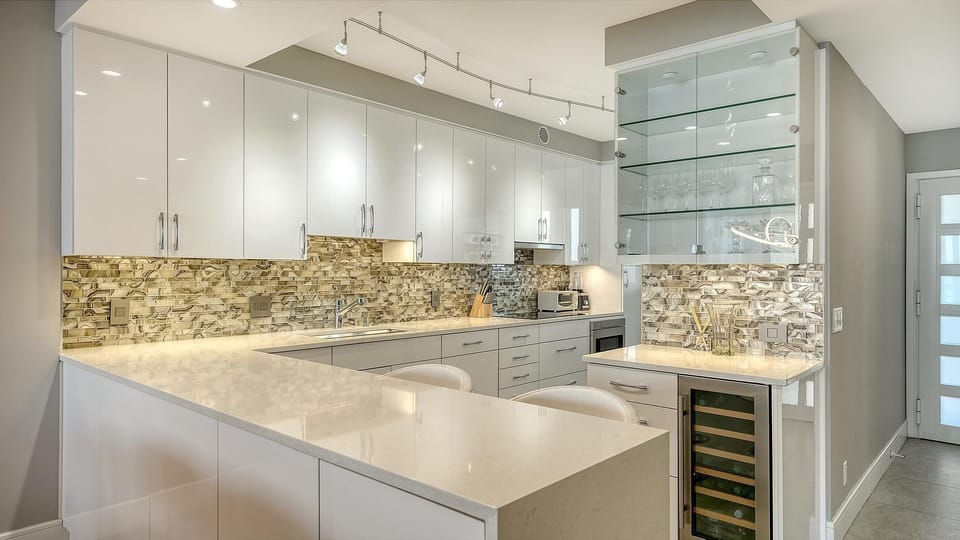 Kitchen with glossy white cabinets, marble countertops, glass-front shelving, and a built-in wine cooler.