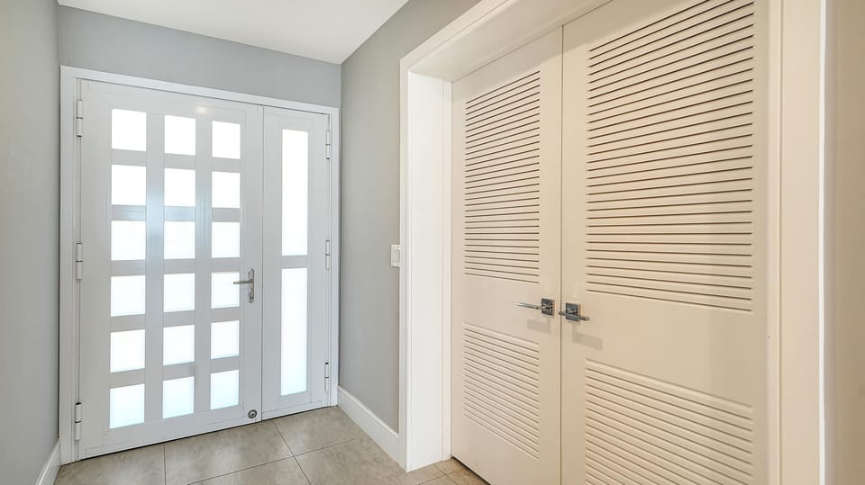 Entryway with frosted glass panel door, light gray walls, beige tile floor, and white louvered closet doors.