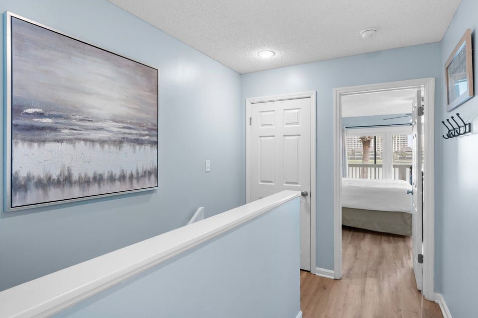 Upstairs hallway with soft coastal tones and wood flooring leads to serene bedrooms—creating a calm transition between living and sleeping spaces.