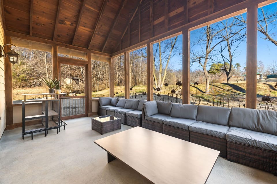 This screened in porch has view of the creek, a large cozy couch, and a bar kart!