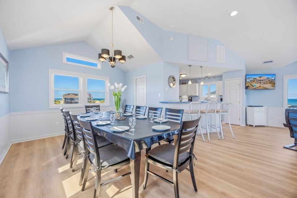 Picture yourself gathering for meals in this airy dining space with soaring ceilings and ocean views framing your stay. Coastal blues and ample seating create a welcoming spot for shared moments.