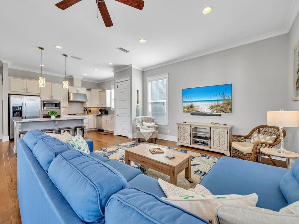 Relax in your bright, open living space with coastal blue sofas and a fully equipped kitchen featuring modern appliances and breakfast bar seating.