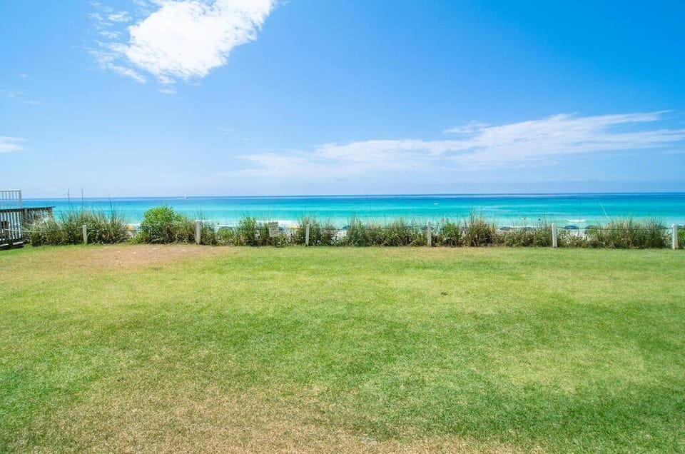 Pristine beachfront property featuring expansive green lawn leading directly to stunning turquoise waters and sandy beach access.