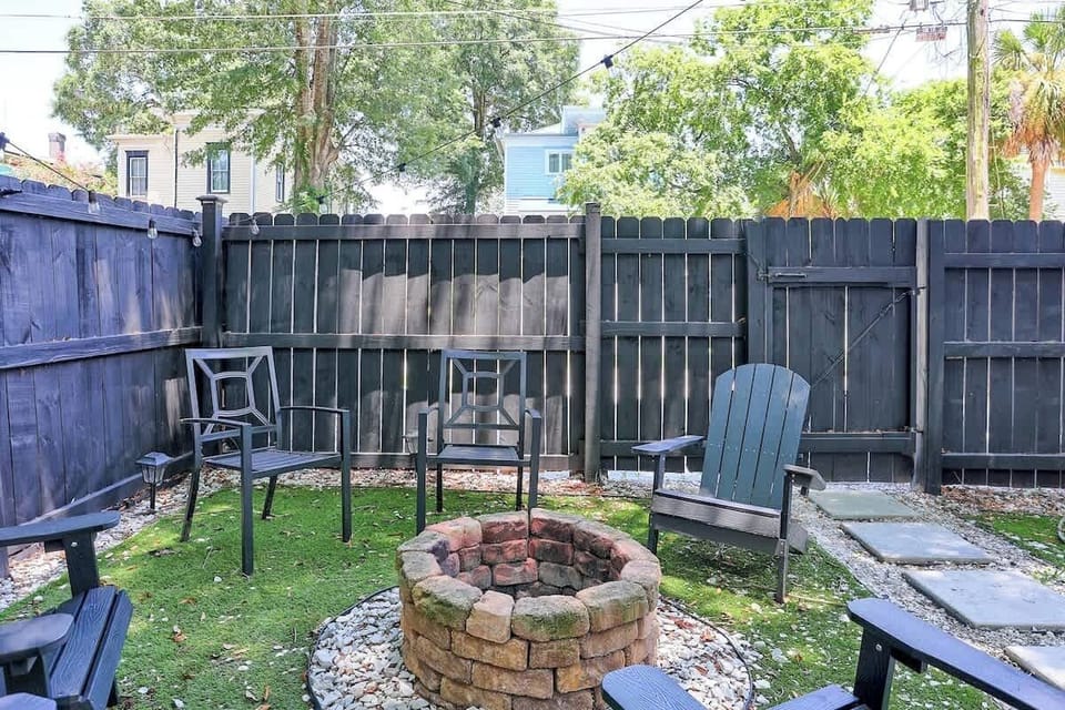 Stone fire pit with Adirondack chairs and metal patio chairs inside the black wood privacy fence.