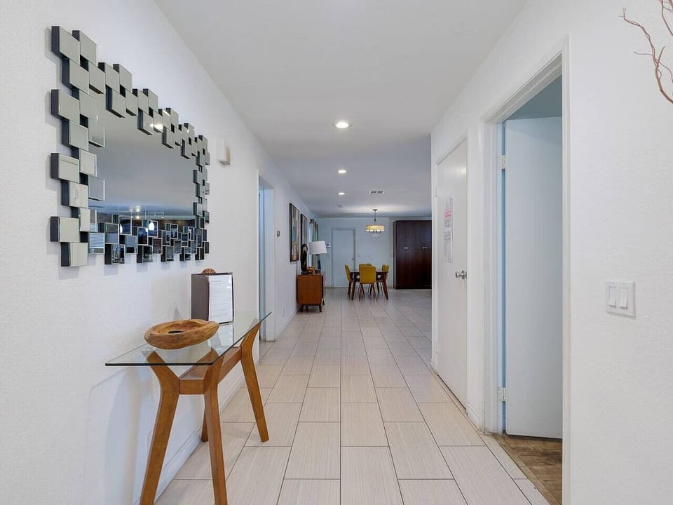 Welcome guests with this stylish entryway featuring a modern mirror, sleek glass console table, and a bright, spacious hallway leading to the living areas.