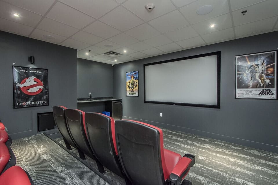 Experience the ultimate movie night in our private home theater, featuring comfortable stadium-style seating, a large projection screen, classic movie posters, and a convenient wet bar for snacks and drinks.