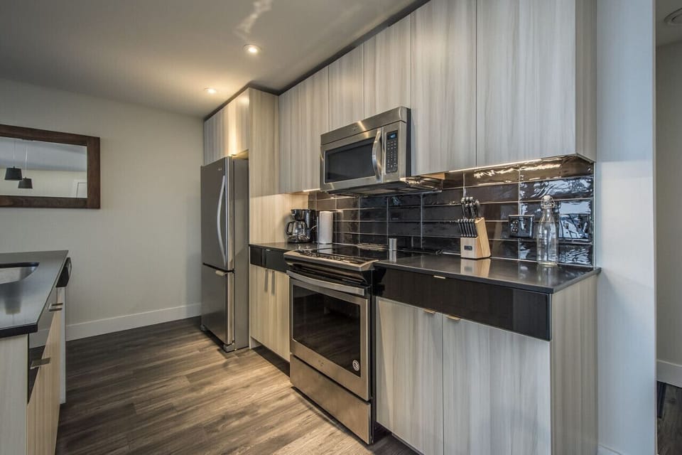 Enjoy preparing meals in this fully equipped contemporary kitchen, highlighting stainless steel Whirlpool appliances, sleek dark granite countertops, glossy black tile backsplash, and elegant light wood cabinetry.