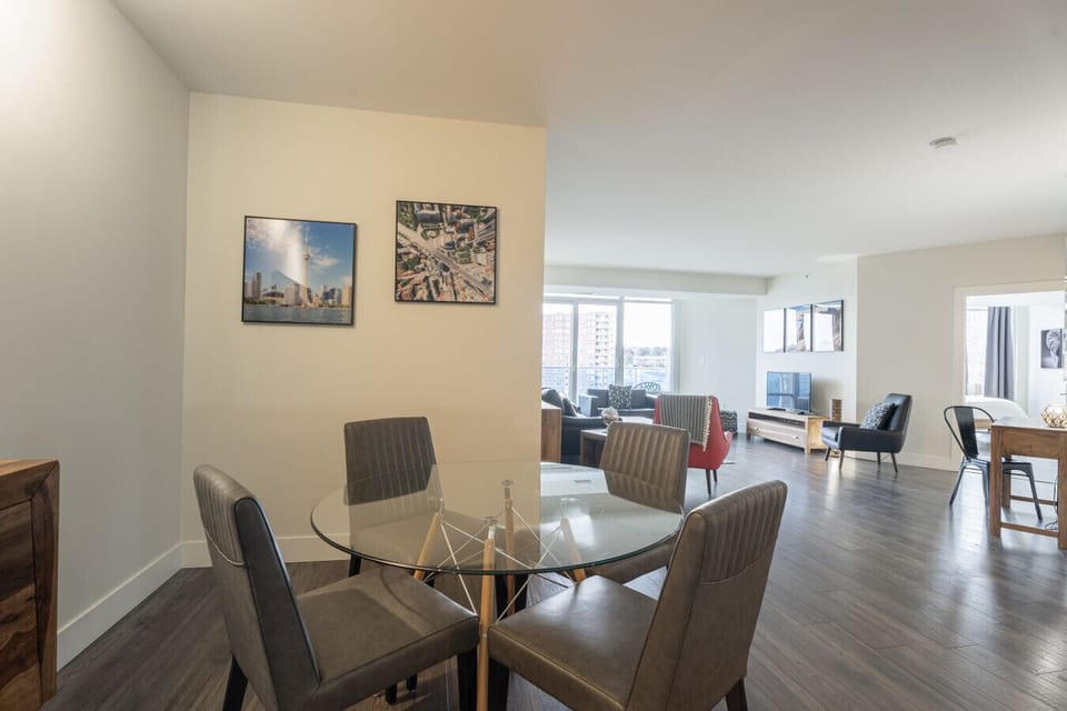 Gather around the glass-top table for a home-cooked meal or your favorite takeout. This inviting dining space, featuring comfy modern chairs, transitions seamlessly into the light-filled living area and balcony—perfect for entertaining.