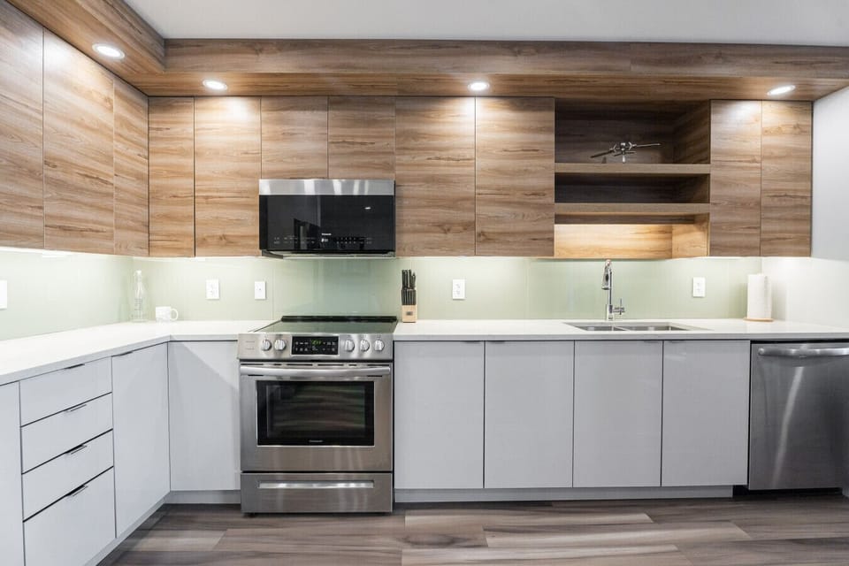 `Sleek custom kitchen featuring rich wood upper cabinets with open shelving, crisp white lower cabinetry, stainless steel appliances, and soft under-cabinet lighting.`
