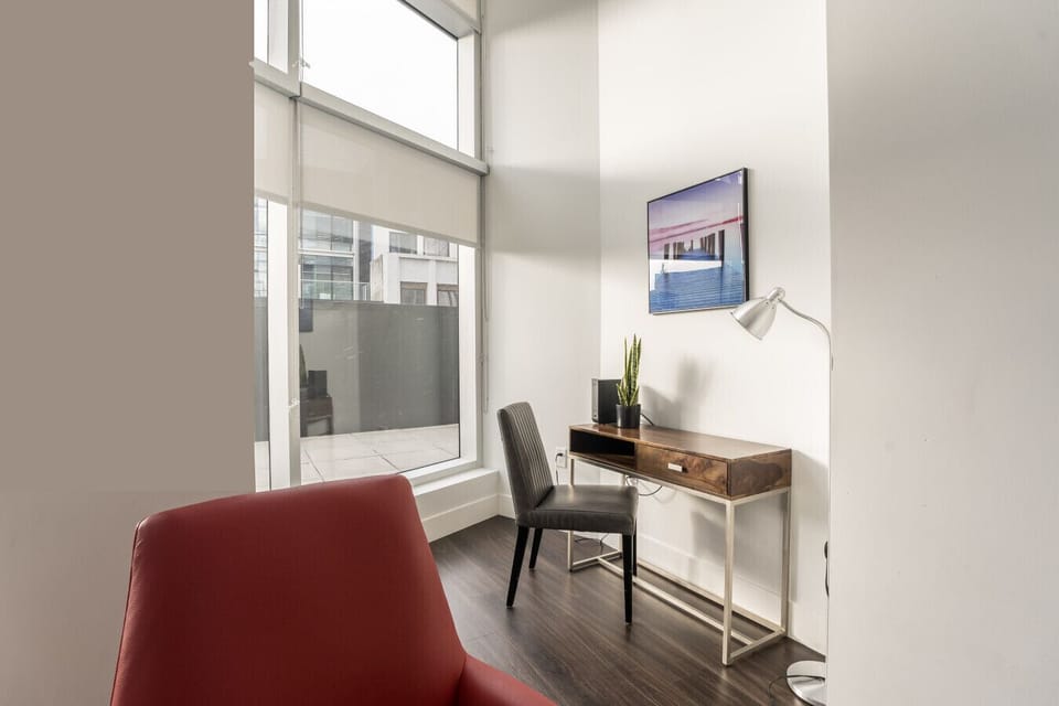 Dedicated workspace bathed in natural light. Features a solid wood desk, comfortable leather chair, adjustable reading lamp, and floor-to-ceiling windows—ideal for remote work or productivity on the go.