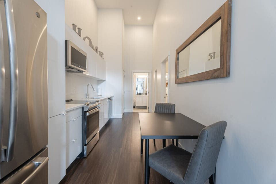 Sleek and functional layout featuring a fully equipped modern kitchen with stainless steel appliances, crisp white cabinetry, high soaring ceilings, and a dedicated dining nook—perfect for cozy meals at home.
