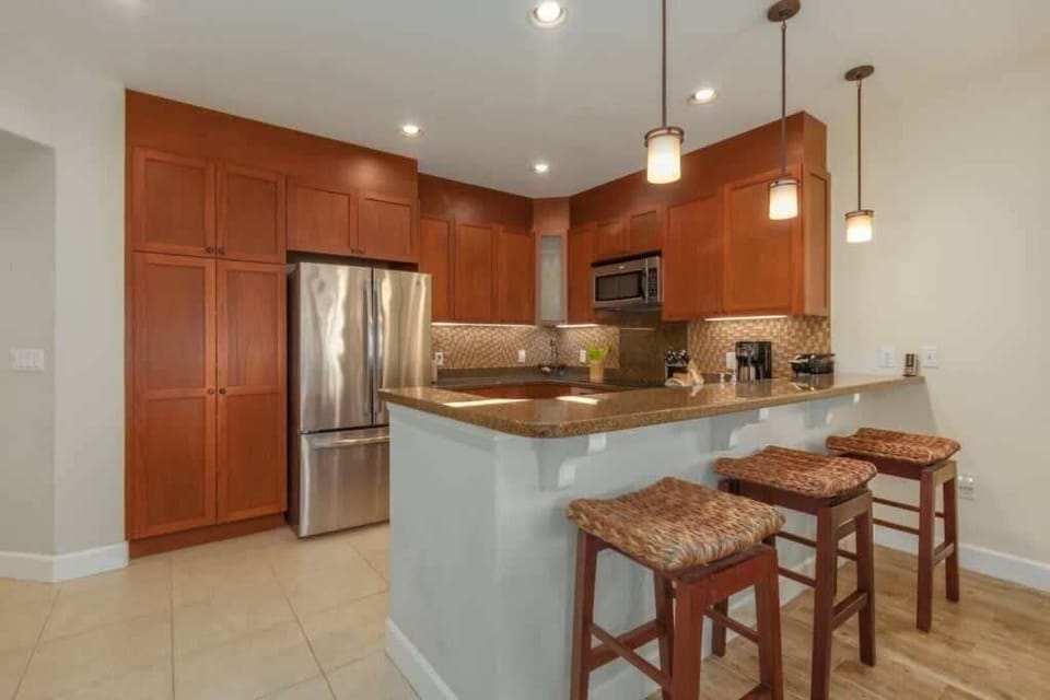 Cook, sip, and mingle at this sleek island kitchen with warm wood cabinets and glowing pendant lights.