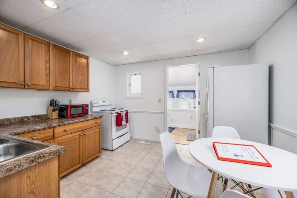 Spacious eat-in kitchen equipped with warm wood cabinetry, durable tile floors, and a breakfast table. Includes full-size appliances and basic essentials for easy home-cooked meals.