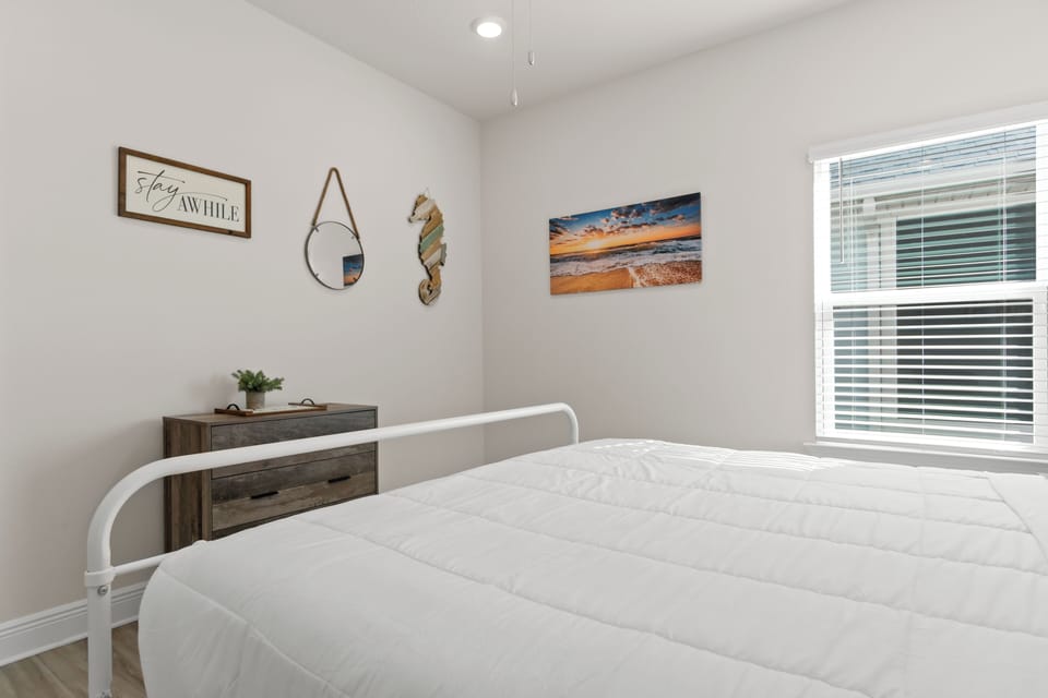 Relax in your peaceful bedroom with coastal artwork and natural light streaming through the window blinds.