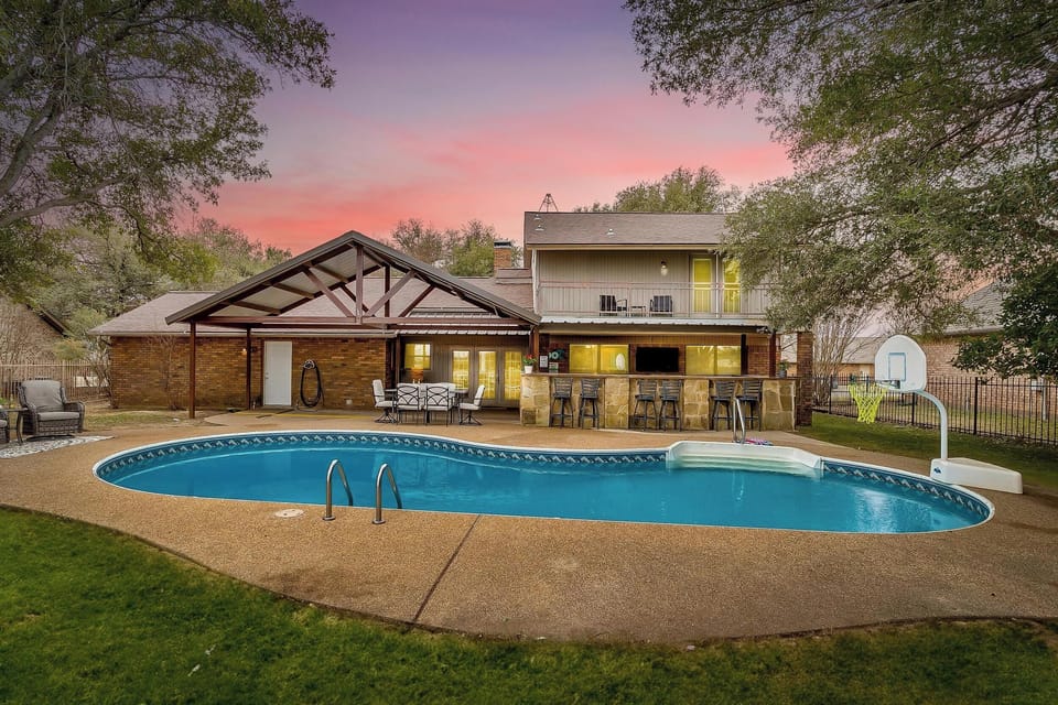 Relax in your private backyard oasis featuring a sparkling pool with a basketball hoop, surrounded by lush greenery and views of the golf course. Perfect for family fun or peaceful retreats