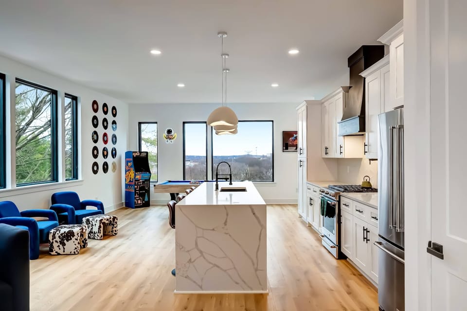 Game room flows straight into the kitchen island and dining area. The cook stays part of the action while others rack up pool or arcade wins nearby