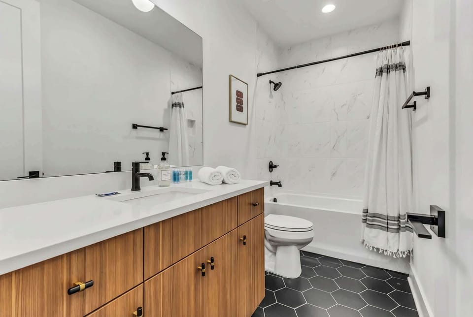 Black hexagonal tile and marble-look shower surround give this full bathroom a motel-modern edge that nods to Nashville's vintage style