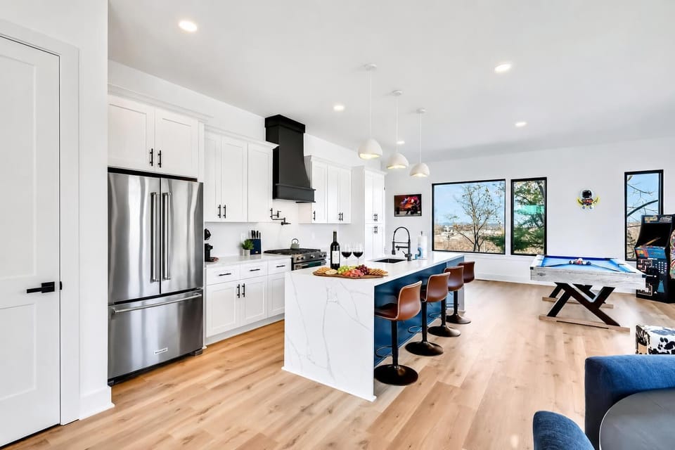 The kitchen is built for groups to cook and hang at the same time. White cabinetry, stainless steel appliances, and island seating keep everyone circling back to the center of the action