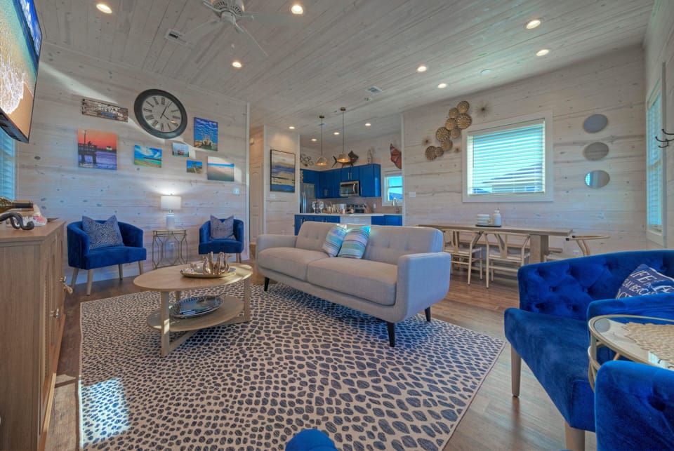 Bright, beach-inspired living room with cozy seating, coastal décor, and a wall-mounted TV—perfect for relaxing after a day in the sun.
