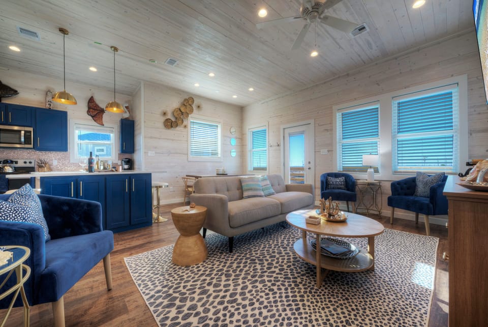 Bright, beach-inspired living room with cozy seating, coastal décor, and a wall-mounted TV—perfect for relaxing after a day in the sun.