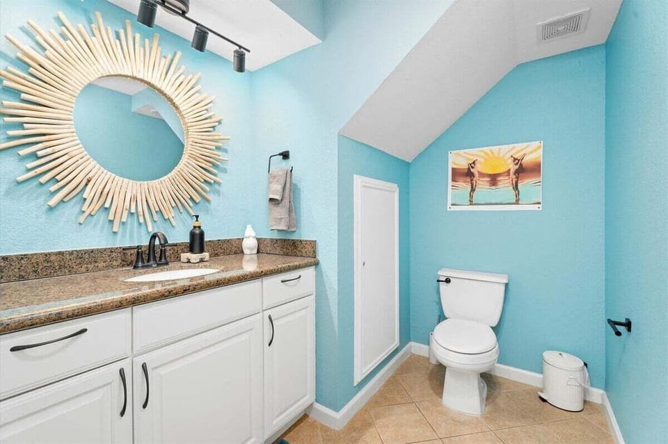 Full bathroom with large vanity, granite countertop, decorative mirror, and bright coastal design.