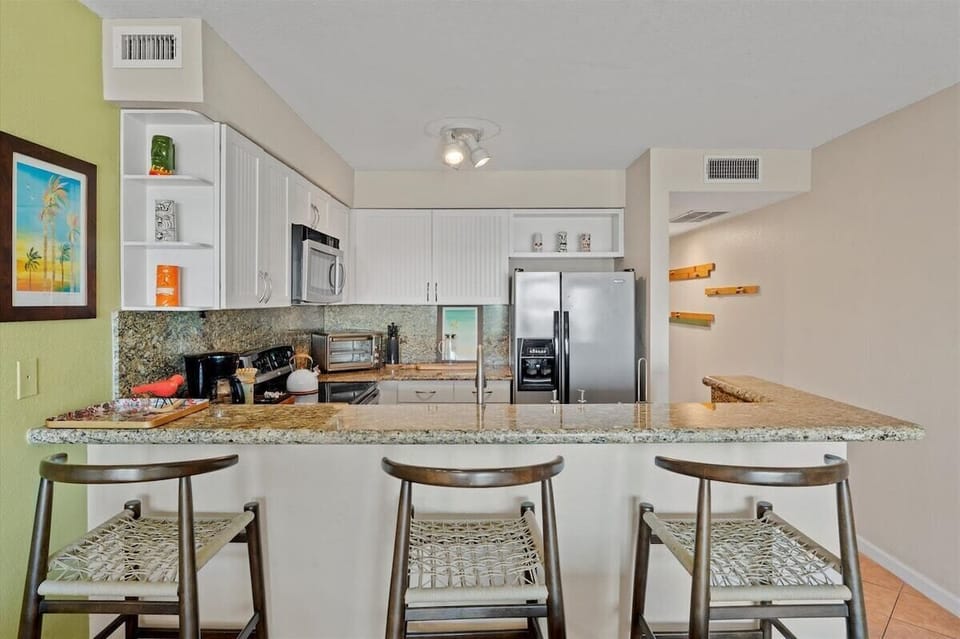 Fully equipped kitchen with granite countertops, stainless steel refrigerator, breakfast bar seating, and open dining space.