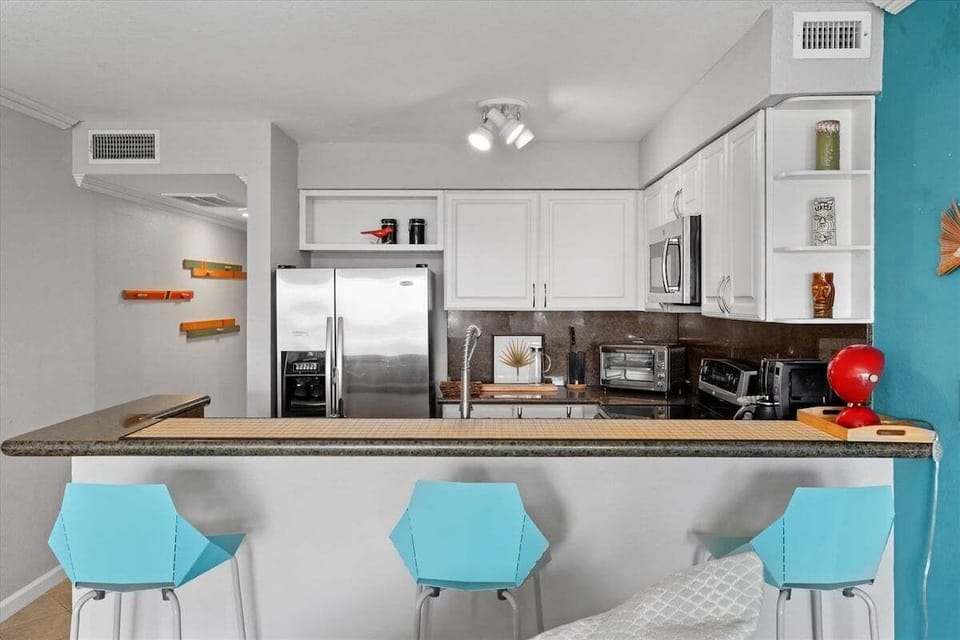 Fully equipped kitchen with stainless steel refrigerator, microwave, oven, breakfast bar seating, and ample counter space for preparing meals and snacks.