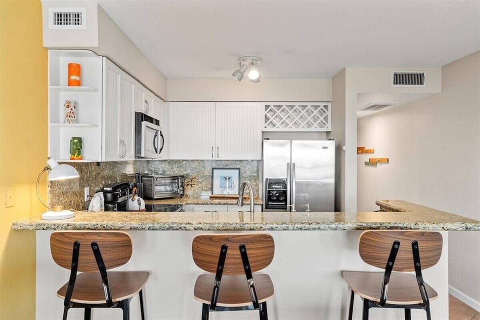 Kitchen breakfast bar with granite counter, bar stools, stainless refrigerator, microwave, and wine rack.