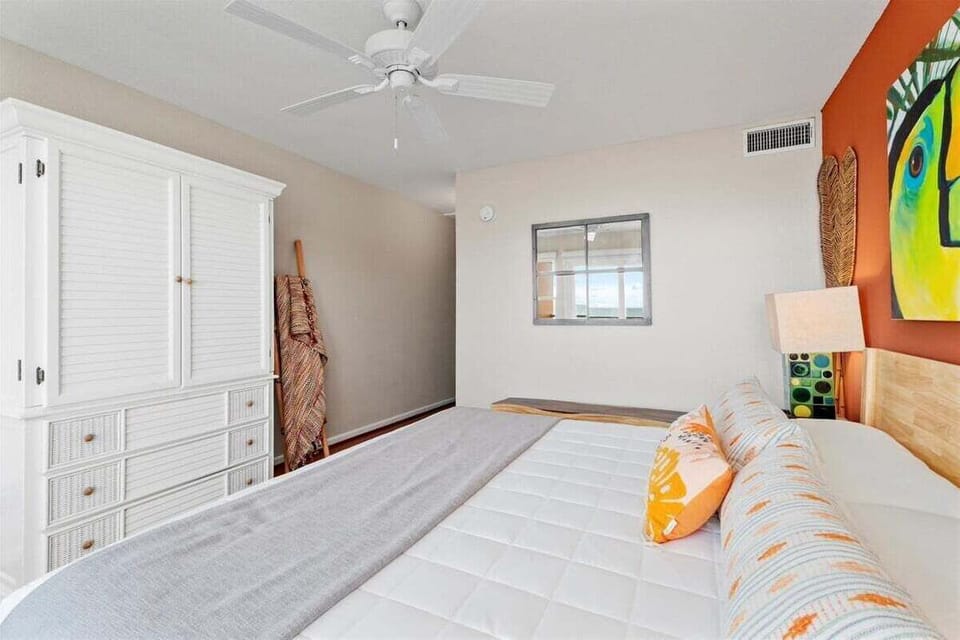 Bedroom with white wardrobe, ceiling fan, large bed, and bright coastal decor.
