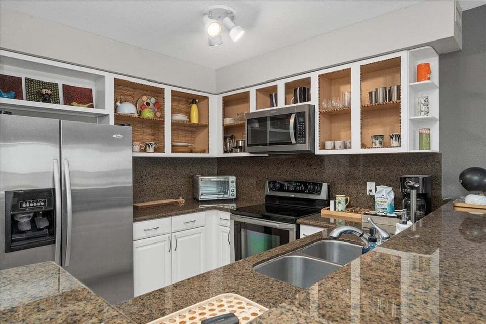 Bright kitchen with stainless refrigerator, microwave, oven, coffee maker, toaster, and open shelving.