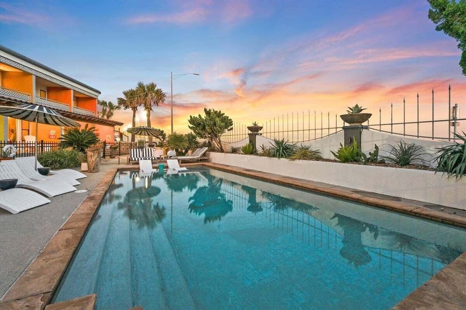 Resort-style pool at sunset with lounge chairs, palm trees, and inviting Galveston vacation atmosphere.