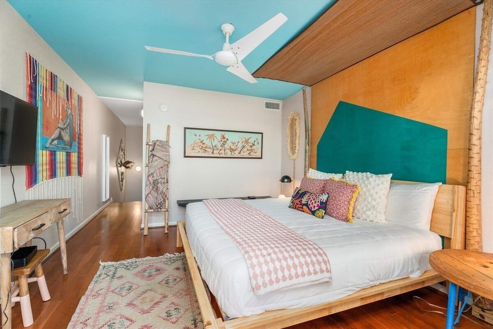 Spacious primary bedroom with king bed, ceiling fan, hardwood flooring, and stylish décor designed for a relaxing stay.