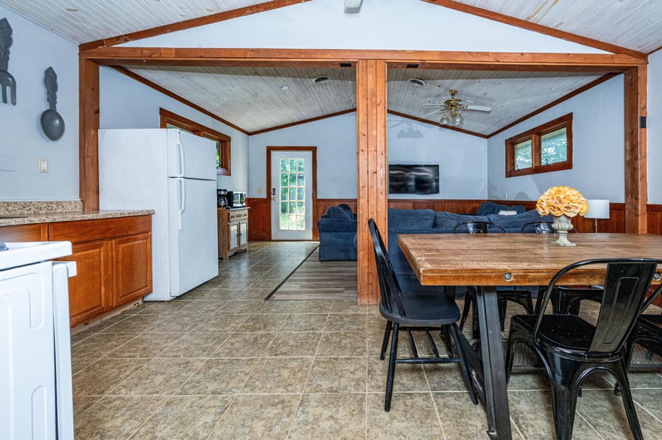 Open-concept dining and living area with wood-paneled accents, tile flooring, and a wall-mounted TV.